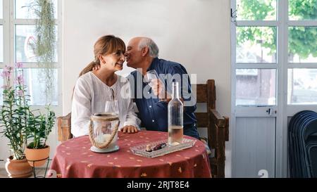 Glücklicher älterer Mann, der Frau umgibt, die im Restaurant sitzt Stockfoto
