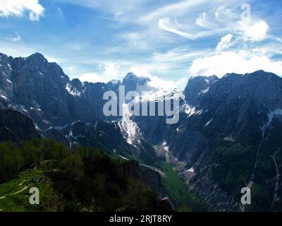 Scenic view of Jalovec mountain and Tamar valley bellow with snow covering the slopes and forest bellow in green foliage and the top covered in clouds Stockfoto
