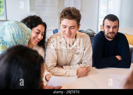 Lächelnder Schüler, der mit Freunden im Klassenzimmer sitzt Stockfoto