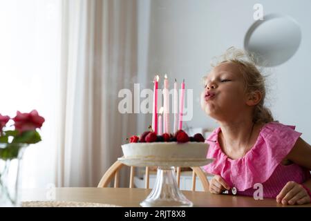 Blondes Mädchen bläst zu Hause Geburtstagskerzen Stockfoto