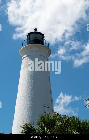 Ein malerischer weißer Leuchtturm, der inmitten üppiger, grüner Bäume an einem leuchtend blauen Himmel steht Stockfoto