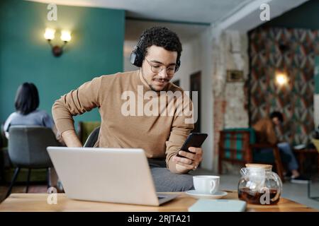 Geschäftsmann, der ein Mobiltelefon nutzt und kabellose Kopfhörer im Café trägt Stockfoto