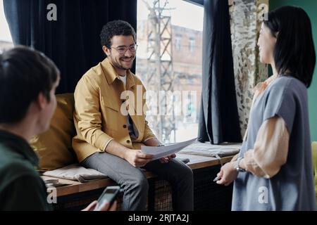 Glücklicher junger Geschäftsmann, der mit Dokumenten sitzt und im Café diskutiert Stockfoto