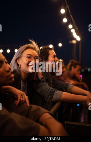 Fröhliche Freunde treffen sich unter Lichterketten auf dem Dach Stockfoto