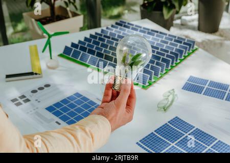 Hand eines Geschäftsmannes, der eine Glühbirne über dem Modell der Solarpaneele hält Stockfoto