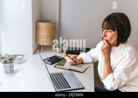 Besinnlicher Freiberufler mit Laptop am Schreibtisch Stockfoto