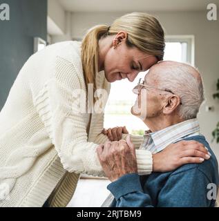 Lächelnde blonde Frau, die sich um ihren Vater zu Hause kümmert Stockfoto