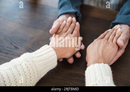 Älterer Mann, der die Hände einer Tochter am Tisch hält Stockfoto