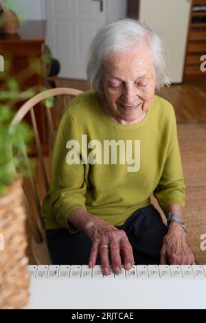 Ältere lächelnde Frau, die zu Hause Klavier spielt Stockfoto
