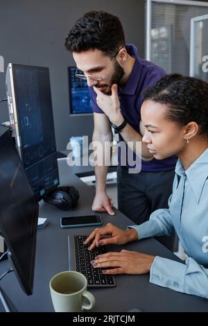 Junger Computerprogrammierer mit Kollegen, die auf der Tastatur am Schreibtisch tippen Stockfoto