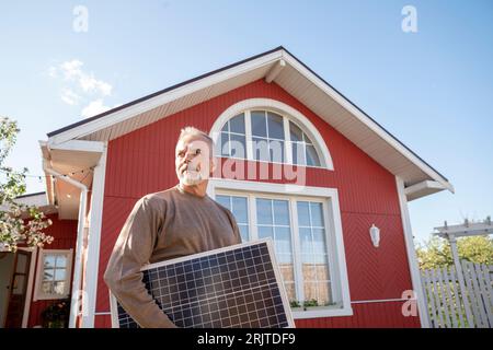 Mann mit Solarmodul vor dem Haus Stockfoto