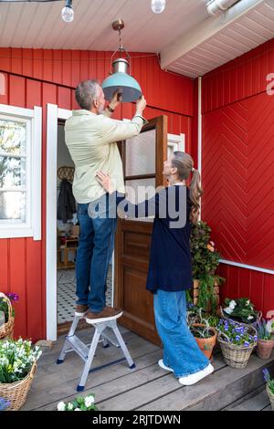 Frau, die bei einem Mann steht und die Glühbirne vor dem Haus wechselt Stockfoto
