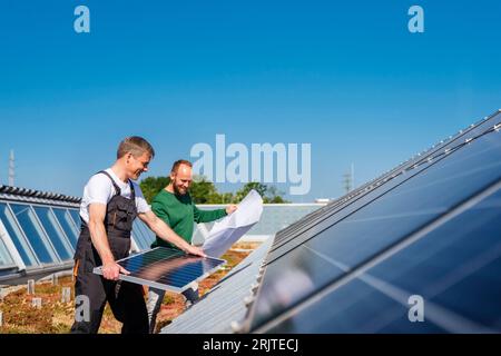 Handwerker installiert Solarpanel auf dem Dach eines Firmengebäudes mit Mitarbeiterplan Stockfoto