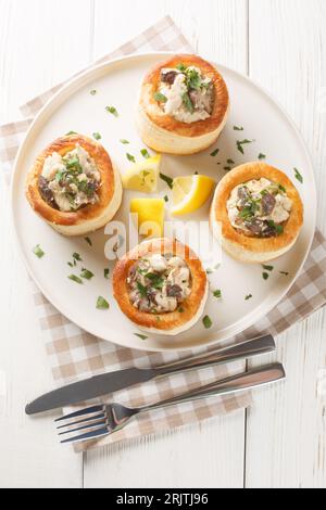 Französische Blätterteigfüllung Vol au Vent mit Hühnchen, Sahne und Pilzcloseup auf dem Teller auf dem weißen Holztisch. Vertikale Draufsicht von oben Stockfoto