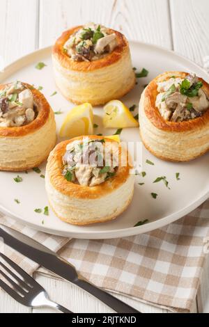 Vol au Vent gebackenes Blätterteig mit Hühnchen, Pilzen und Sahne auf dem Teller auf dem weißen Holztisch. Vertikal Stockfoto