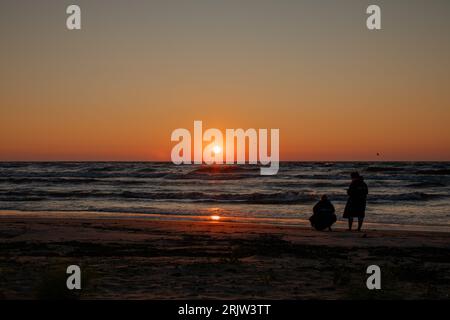 A duo watches as the sun sets over the wind-whipped waves of Lake Huron Stock Photo