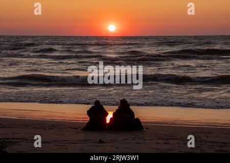 A duo watches as the sun sets over the wind-whipped waves of Lake Huron Stock Photo