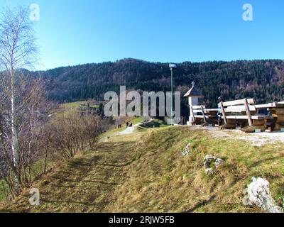 Gravel path leading across a ridge from the church at Jamniki bellow Jelovica in Gorenjska, Slovenia with wooden benches in front and woods in the bac Stock Photo