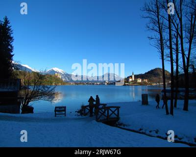 Blick auf den See Bled mit einem bewaldeten Hügel im Rücken und einem schneebedeckten Gipfel der Karawanken mit Stol in der Mitte der Gorenjska Region Slo Stockfoto