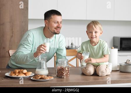 Glücklicher kleiner Junge und sein Vater mit verschiedenen Gebäckstücken, der Milch in der Küche trinkt Stockfoto