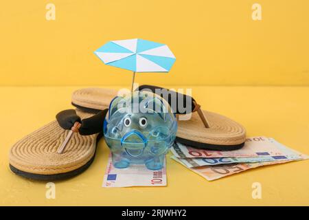 Schweinebank mit Geld und Strandaccessoires auf gelbem Hintergrund. Konzept der Reisekostenersparnis Stockfoto