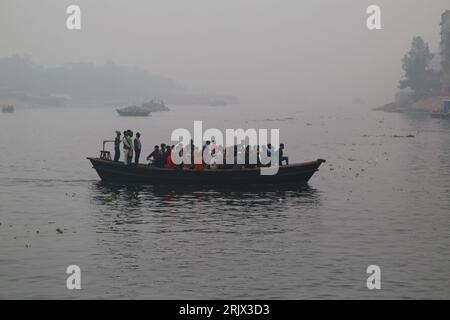 DHAKA, BANGLADESCH-20. JANUAR: Die Menschen fahren in einem Boot, während sie den Shitalakhaya River an einem nebligen Morgen in Narayanganj bei Dhaka, Bangladesch, am 20. JANUAR 2021 überqueren. Stockfoto