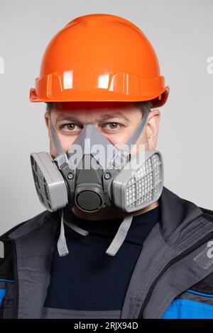 Ein Mann mit Schutzhelm und Atemschutzmaske zum Schutz vor Staub und Gasen auf weißem Hintergrund. Stockfoto