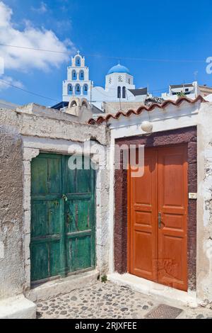 Bunte traditionelle Holztüren nebeneinander, mit der Kuppel und dem Glockenturm des Dorfes im Hintergrund, in Pyrgos Kallistis, Santorin. Stockfoto