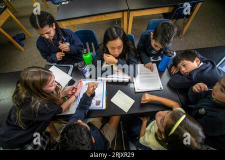 Uniformierte multirassische Schüler einer katholischen Mittelschule in Südkalifornien diskutieren die Bücher, die sie als Gruppe im Klassenzimmer gelesen haben. Stockfoto