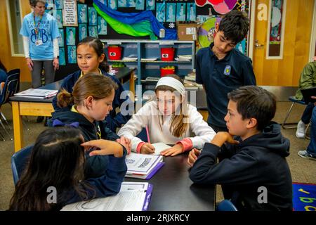 Uniformierte multirassische Schüler einer katholischen Mittelschule in Südkalifornien diskutieren die Bücher, die sie als Gruppe im Klassenzimmer gelesen haben. Stockfoto