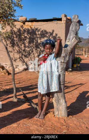 Afrikanisches Kind im Dorf, spielt mit einer Puppe auf der unbefestigten Straße vor dem Haus Stockfoto