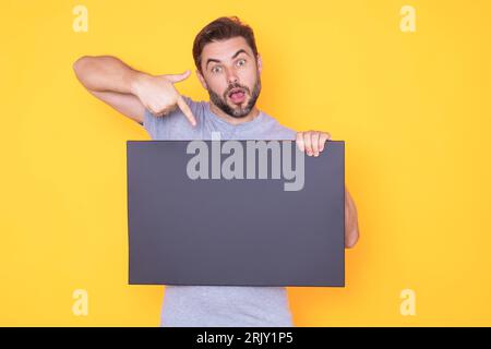 Ein Mann, der Werbung zeigt und mit dem Finger auf eine leere Tafel zeigt, im Studiohintergrund. Leeres Schild mit Textbereich. Werbekonzept. Anzeigetafel mit Stockfoto