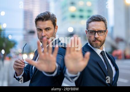 Krise, Risiko. Zwei gutaussehende Geschäftsleute im Anzug hören auf mit der Hand zu singen. Warnausdruck mit negativer und ernsthafter Geste im Gesicht. Halt die Hand an Stockfoto