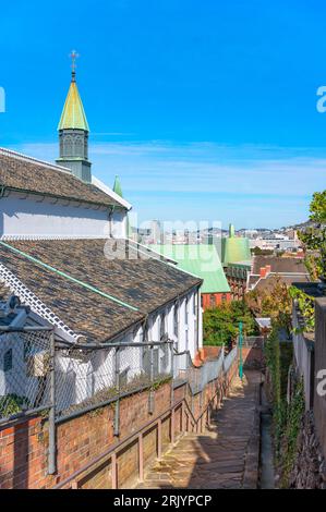 Schmale Steigung der Kopfsteinpflastertreppe Kinenzaka, die entlang der japanischen Shikkui-Gipsmauern der Basilika der sechsundzwanzig Heiligen Märtyrer von Japan hinuntergeht Stockfoto