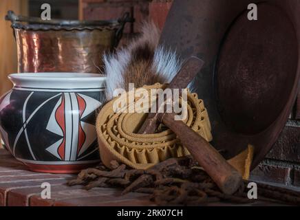 Herd aus roten Ziegeln zeigt indianische Keramik, Kartuschenriemen, Hirschschwanz, Goldpfanne, Pick Axt und rostige Kette aus der alten Westzeit. Stockfoto