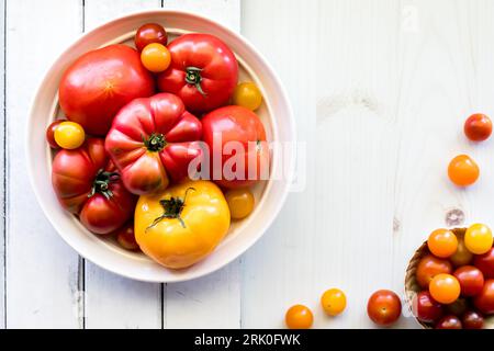 A bowl full of tomatoes on a white rustic board with copy space to the right. Stock Photo