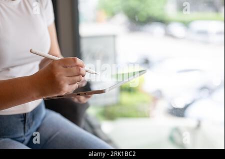 Nahaufnahme einer Frau, die ihr Tablet benutzt, während sie in einem Café sitzt. Freiberufler, digitaler Nomad, Fernarbeit Stockfoto