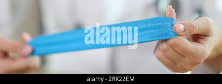 Physiotherapeutin zeigt blaue medizinische Klebebänder in den Händen, während sie am Tisch in der medizinischen Klinik sitzt. Stockfoto