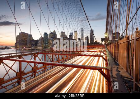Der Blick auf das Finanzviertel in New York City hinter dem Verkehr auf der Brooklyn Bridge nach Sonnenuntergang. Stockfoto