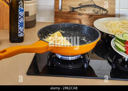 Morgens gesundes Frühstück mit Rührei mit Parmesankäse, Gurken, Kirschtomaten und Gemüsepaprika wird in der Pfanne auf einem Gasofen gebraten. Stockfoto