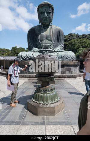 Ein Besucher des Tempelgeländes von Kamakura in Japan reinigt sich mit Rauch von brennendem Weihrauch vor einem 40 m hohen Bronzeskulptur Buddha. Stockfoto