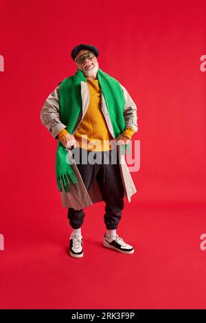 Foto in voller Länge von positivem, entzückendem Seniorenmann mit einem Bart in einem hellen Outfit und Brille mit Händen auf Hüften, die vor Glück tanzen. Stockfoto