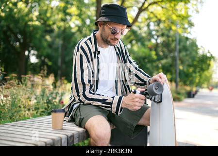 Ein eleganter Erwachsener, der sein Skateboard im Skatepark repariert. Skateboard-Schlüssel Stockfoto