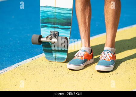 Close-up of male legs in sneakers standing with skateboard on a yellow and blue concrete platform, summer vibe Stockfoto