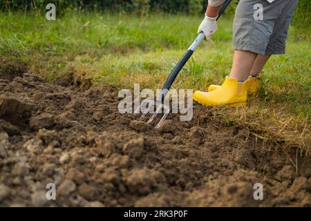 Landwirt, der mit Handwerkzeugen Land im Garten anbaut. Bodenlockerung. Gartenkonzept. Rechen und Spaten auf gelöstem Boden. Landwirtschaftliche Arbeiten Stockfoto