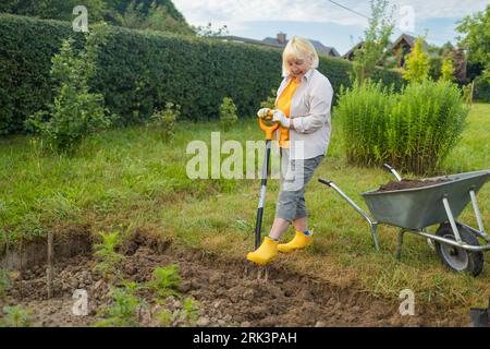 Landwirt, der mit Handwerkzeugen Land im Garten anbaut. Bodenlockerung. Gartenkonzept. Rechen und Spaten auf gelöstem Boden. Landwirtschaftliche Arbeiten Stockfoto