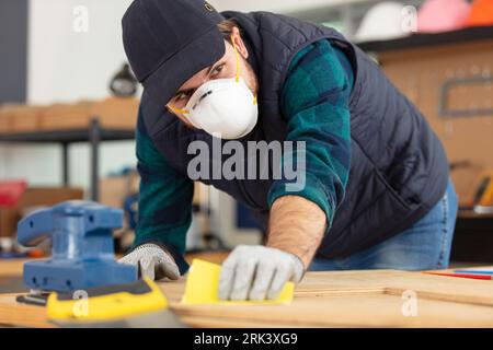 Junger Zimmermann, der in seiner Holzwerkstatt mit Maske steht Stockfoto