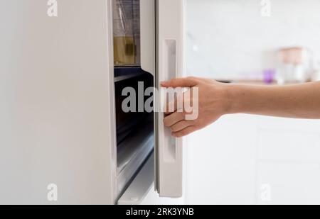 Female hand opening white refrigerator door Stock Photo