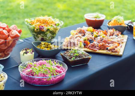 A table is set with delicious snacks prepared for a buffet in the garden. A board with charcuterie, fresh vegetables, vegetable salads, salsa Stock Photo