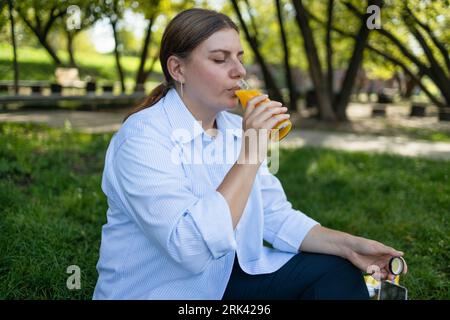 Lifestyle Junge Frau trinkt frisch gepressten selbstgemachten Orangensaft im städtischen Sommerpark Stockfoto